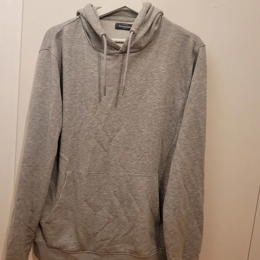 Säljer en stilren och bekväm grå hoodie från Dressmann i storlek L. Perfekt för både vardag och chill. Den har en klassisk design med snören i huvan och en ficka fram. Passar perfekt till höst och vår!. Tröjor & Koftor.