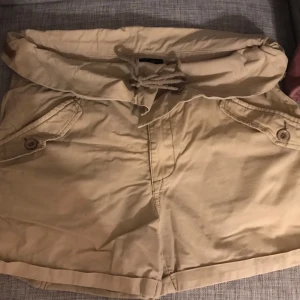 Beige shorts från Sisters Point - Snygga beige shorts från Sisters Point i storlek L. De har en bekväm loose passform med knappar och snörning i midjan. Perfekta för sommardagar eller en avslappnad vårlook. Materialet känns som bomull och de har praktiska fickor framtill.