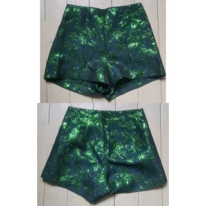 Högmidjade skimrande shorts 38 - Nyskick. 80% polyester, 20% "metallised fiber". Basen är marinblå typ, men ser svart ut i de flesta ljus. Blixtlås bak och två fickor. Midjevidd: 35, stussvidd: 56, längd: 33,5