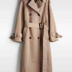 Beige trenchcoat - Snygg beige trenchcoat i klassisk stil med dubbelknäppning och bälte i midjan. Perfekt för höst och vår. Långärmad med justerbara spännen vid ärmsluten för en skräddarsydd passform. Ett måste i garderoben för en stilren look!