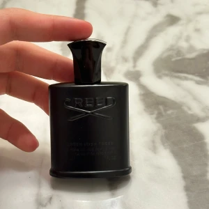 Svart parfymflaska från Creed - Säljer en elegant svart parfymflaska från Creed. Flaskan har en stilren design med en matt finish och ett snyggt lock. Perfekt för den som gillar lyxiga dofter och vill ha en stilfull flaska på hyllan. Passar både till vardags och fest! Helt ny köpt 2 dagar sen 