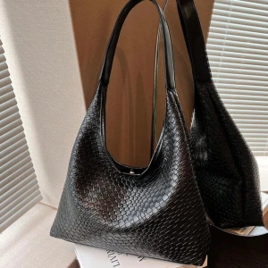 Svart axelväska i flätat mönster - Snygg svart axelväska med ett elegant flätat mönster. Perfekt för både vardag och fest. Väskan har en stilren design med bekväma axelremmar. Passar till alla outfits och ger en lyxig touch.