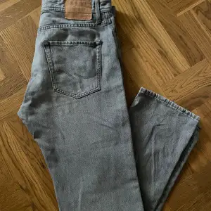 Säljer ett par grå jeans från Jack & Jones i modellen Relaxed Chris. De har en avslappnad passform och är perfekta för en casual look. Jeansen har en klassisk femficksdesign och knappar i silver. Storlek 30/30