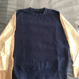 Blå tröja med vit/beiga ärmar från French Connection - Säljer en snygg blå/vit/beige tröja från French Connection i storlek S. Tröjan har långa ärmar med en cool färgblock-design i beige och vit. Perfekt för en avslappnad stil och passar bra till både jeans och chinos.