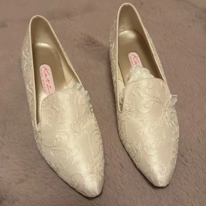 Eleganta broderade skor från Katz - Säljer ett par eleganta skor i siden från Katz i en vacker krämfärg. Skorna har en spetsig tå och är dekorerade med ett intrikat broderat mönster. Perfekta för speciella tillfällen som bröllop, studenten eller bal. De är helt oanvända och har en liten klack för extra komfort.