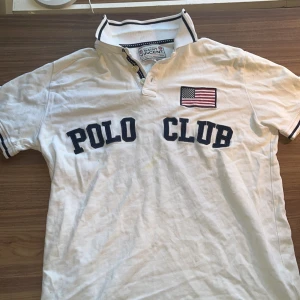 Vit Pike - Säljer en klassisk vit pikétröja från Saint Vincent 'POLO CLUB' . Tröjan har en amerikansk flagga broderad på bröstet och en snygg krage med svarta ränder. storlek S, 175 cm. färg vit och svart. bra skick. hör av dig vid mer frågor 