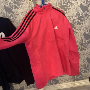 Rosa långärmad tröja från Adidas - Säljer en snygg och sportig rosa långärmad tröja från Adidas. Den har en halv dragkedja framtill och de klassiska tre svarta ränderna längs ärmarna. Perfekt för träning eller en avslappnad dag. Tröjan är i bra skick, typ oanvänd och redo för nya äventyr!