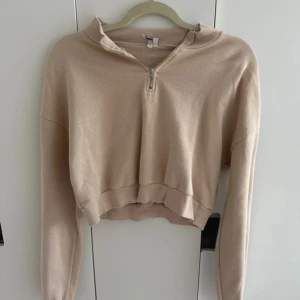 Beige croppad tröja med dragkedja - Säljer en superfin beige croppad tröja med dragkedja framtill. Den är perfekt för en avslappnad stil och har långa ärmar. Materialet känns mjukt och skönt, perfekt för både vår och höst. 