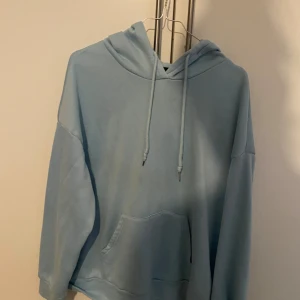 Ljusblå hoodie med tryck - Säljer en supermysig ljusblå hoodie med ett coolt gult tryck på baksidan som säger 'LOVE YOU EVERY MINUTE'. Den har en klassisk känguruficka och justerbar huva med dragsko. Perfekt för chilliga dagar eller när du vill sprida lite kärlek! 💙💛