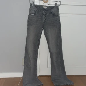 Grå jeans med knappar - Säljer ett par grå jeans med en cool vintage-look. De har en knappgylf och är i bootcut-stil, vilket ger dem en skön retro vibe. Perfekta för både vardag och fest! 🖤