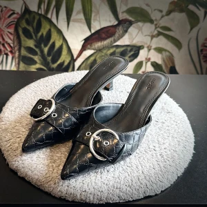Coquette kitten-klack med spetsig tå - Svarta slip in kitten heel klackar från NA-KD med metallspänne-detalj på tå  Väldigt preppy och coquette  Stl 39  Helt nya aldrig använda