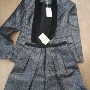 Nytt Sett från Just Addict  - Säljer en superglittrig kavaj och matchande kjol från Just Addict. Perfekt för nyårsfesten eller en glammig utekväll! Kavajen har en klassisk passform med svarta slag och långa ärmar. Kjolen är kort och har en bekväm resår i midjan. Båda plaggen är i en snygg silverfärg som verkligen fångar ljuset.