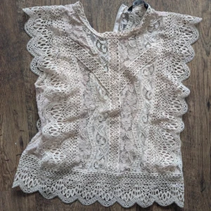 Beige rosa spetsblus - Säljer en superfin vit/ beige/rosa spetsblus med vackra detaljer. Blusen har spetsvolang kanter och har ett intrikat spetsmönster som ger en romantisk känsla. Perfekt för sommarens alla fester eller en dag på stan!