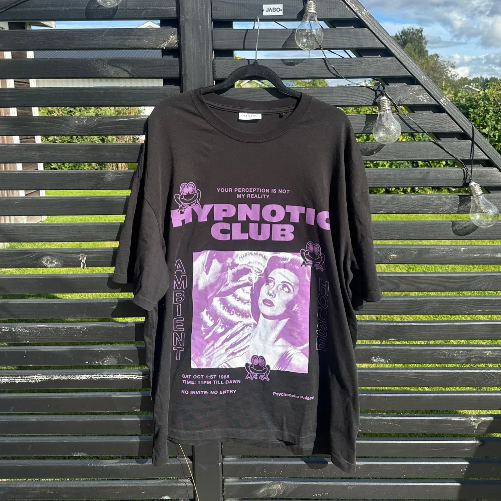 Säljer en cool svart t-shirt från Vailent med ett stort lila tryck på framsidan. Texten 'HYPNOTIC CLUB' och en retroinspirerad bild ger den en unik look. Perfekt för en avslappnad stil eller en utekväll. T-shirten är i bra skick och har korta ärmar. t-shirten är oversized. T-shirts.