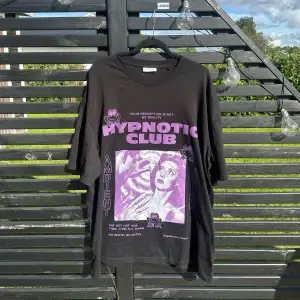 Säljer en cool svart t-shirt från Vailent med ett stort lila tryck på framsidan. Texten 'HYPNOTIC CLUB' och en retroinspirerad bild ger den en unik look. Perfekt för en avslappnad stil eller en utekväll. T-shirten är i bra skick och har korta ärmar. t-shirten är oversized