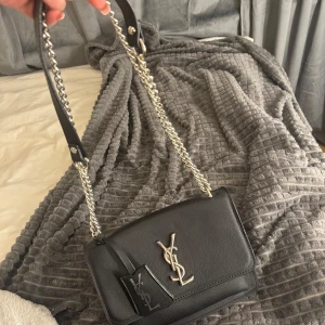 Svart axelväska med kedja - En falsk YSL väska från Turkiet som aldrig kommit till använd! Väskan har en dragkedja inuti och är perfekt för både vardag och fest. Den är i mycket bra skick och har en stilren design som passar alla tillfällen. Pris kan diskuteras!