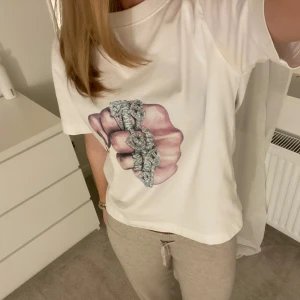 Vit t-shirt med tryck - Säljer en vit t-shirt med ett coolt tryck av en hand med smycken. Tjejen jag köpte av här på Plick har gjort trycket själv och är skit snyggt! Har liten defekt vid armhålorna men som inte syns när man har på sig den.