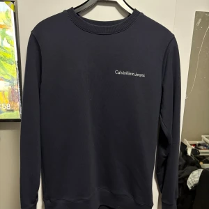 Mörkblå tröja från Calvin Klein Jeans - Snygg mörkblå tröja från Calvin Klein Jeans med diskret logga på bröstet. Tröjan har en klassisk rund hals och långa ärmar, perfekt för en stilren look.