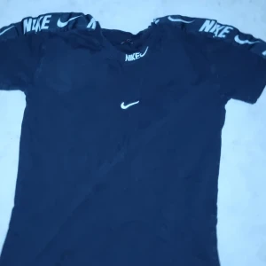 Svart t-shirt från Nike - Snygg svart t-shirt från Nike med korta ärmar och logotyp på bröstet. Perfekt för en sportig look med Nike-märke längs axlarna.