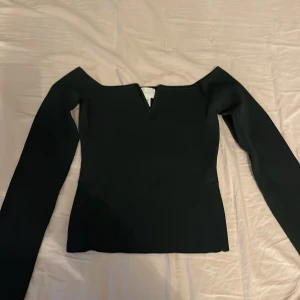 Svart offshoulder topp från H&M - Snygg mörkgrön offshoulder topp från H&M med långa ärmar. Perfekt för en stilren look. Toppen har en elegant design med en liten v-ringning framtill.