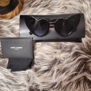 Svarta hjärtformade solglasögon från Saint Laurent - Snygga svarta solglasögon från Saint Laurent med hjärtformade bågar. Perfekta för att ge en trendig touch till din stil. Kommer med originalfodral och putsduk. Modellen heter loulou...självklart äkta....pris: 1000 kr