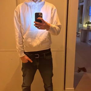 Vit hoodie från Jack & Jones - Säljer en stilren vit hoodie från Jack & Jones. Den har en klassisk design med en stor ficka framtill och justerbar huva. Perfekt för en avslappnad look. En liten blå fläck finns som man inte ser