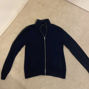 Mörkblå fullzip från Jack & Jones - Snygg mörkblå tröja från Jack & Jones med dragkedja framtill. Perfekt för en stilren look, med långa ärmar och ribbade detaljer vid kragen och ärmsluten. Passar bra till jeans för en avslappnad stil för ett bra pris. Storleken är xs men passsr även s.
