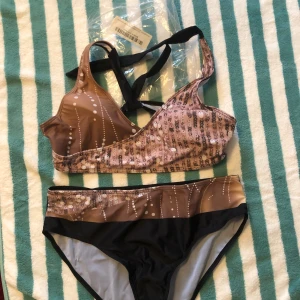 Brun och svart bikini med mönster - Snygg bikini i brunt och svart med unikt mönster. Toppen har breda axelband och en sportig design. Perfekt för en dag på stranden eller vid poolen.