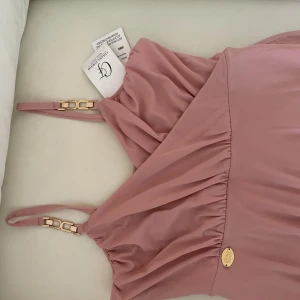 Rosa klänning från Chiara Forthi - Elegant rosa klänning från Chiara Forthi med omlott-design och justerbara axelband med gulddetaljer. Perfekt för en stilfull look.