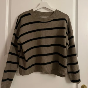 Beige och svart randig stickad tröja - Säljer en mysig beige stickad tröja med svarta ränder. Tröjan har en avslappnad passform och långa ärmar, perfekt för kyligare dagar. Den är enkel att matcha med olika outfits.