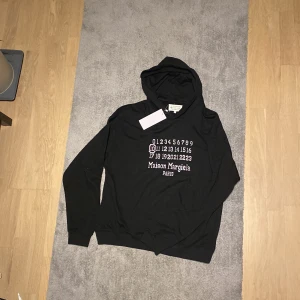 Maison margiela hoodie - Säljer en stilren svart hoodie från Maison Margiela med deras ikoniska nummertryck på framsidan. Den är tillverkad i Italien och har en klassisk passform med långa ärmar och en bekväm huva. Perfekt för både vardag och avslappnade tillfällen. Hoodien är u nyskick med taggar. Mitt pris 2499, nypris runt 6000. Kontakta mig vid vidare funderingar eller frågor.