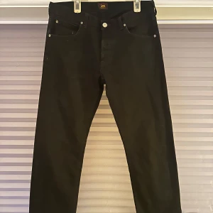 Svarta jeans från Lee - Säljer ett par svarta jeans från Lee i bra skick. De har en klassisk femficksdesign och en knapp med Lee-loggan.  Storleken är 32/32
