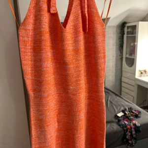 Orange stickad klänning - Trendig orange stickad klänning med smala axelband och en figurnära passform. Perfekt för en färgglad look. Klänningen har en enkel design som gör den lätt att styla.