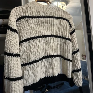 Vit och svart randig stickad tröja - Säljer en mysig vit stickad tröja med svarta ränder. Tröjan har en avslappnad passform och långa ärmar, perfekt för kyliga dagar. Den är både stilren och bekväm, idealisk för höst och vinter.