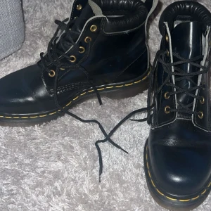Svarta boots från Dr. Martens - Säljer ett par klassiska svarta Dr. Martens boots med snörning och gul söm. Tillverkade i skinn med en robust sula för extra komfort. Perfekta för både stil och funktion. Storlek 6 som motsvarar en liten 39🥰Använda fåtal gånger!