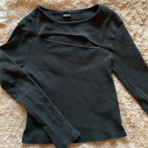 Svart ribbad topp från Gina Tricot - Säljer en svart ribbad topp från Gina Tricot i mycket bra skick. Den har en asymmetrisk öppning framtill och långa ärmar. Strl L men den är mycket liten i strl så den passar Xs-s