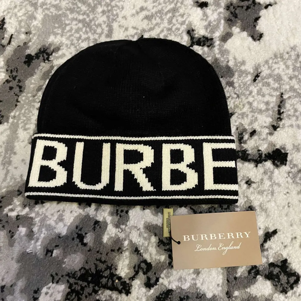 Snygg svart mössa från Burberry med vit text på uppviket. Perfekt för att hålla sig varm och stilren under kyliga dagar. Passar både till vardags och lite finare tillfällen. Utan pris lapp.. Accessoarer.