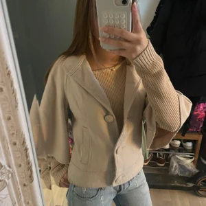 Trekvartsärmad kappa med knappar - Säljer en snygg beige Trekvartsärmad kappa i mycket bra skick. Den har en stilren design med knappar framtill.