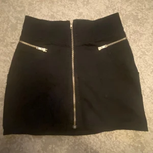 Svart jeanskjol  - En svart jeanskjol med kedjor. Den har två fickor på framsidan men inga på baksidan. Längd: ca 36cm Midjemått rakt över:ca 33cm. Den är i storlek 34.
