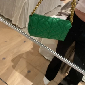 Grön väska från ZARA - Snygg grön väska från ZARA med en cool kedjerem i guld. Väskan är i mycket bra skick och passar både till vardags och fest.
