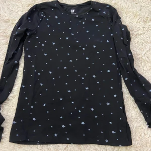Svart långärmad tröja med stjärnor från H&M - Säljer en svart långärmad tröja från H&M med ett coolt stjärnmönster. Tröjan är gjord av ekologisk bomull och passar perfekt nu till jul! 
