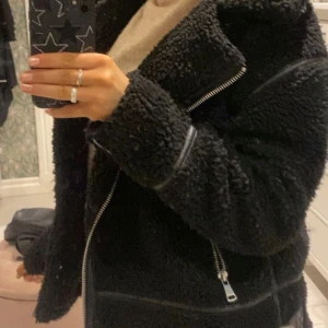 Svart teddyjacka med dragkedja - Mysig svart teddyjacka med dragkedja och långa ärmar. Perfekt för kyliga dagar när du vill hålla dig varm och stilren. Har svarta läder och silver detaljer! Kommer inte riktigt ihåg vart den är ifrån (har klipp bort lappen i) men skulle gissa på ZARA!