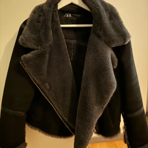 Svart jacka med fuskpäls från Zara - Snygg svart jacka från Zara med mjuk fuskpäls på insidan och kragen. Jackan har dragkedja och är perfekt för kyligare dagar. Den har en modern look med en croppad passform.