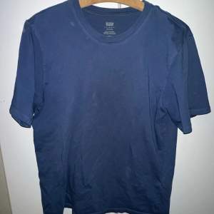 Säljer en snygg mörkblå t-shirt från Levi's i bra skick. Den är gjord av mjuk bomull och har en klassisk rund hals. Perfekt för vardagsbruk eller avslappnade tillfällen. Passar bra till jeans eller shorts!