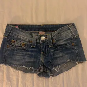 Säljer ett par snygga blå jeansshorts från True Religion i bra skick. De är lågmidjade med slitna kanter och klassiska femficksdesign. Perfekta för sommardagar eller festivaler! 🕶️