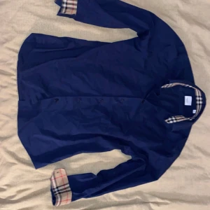 Mörkblå skjorta från Burberry - Snygg mörkblå skjorta från Burberry med klassiska rutiga detaljer på insidan av kragen och ärmsluten. (Står XL men sitter L)
