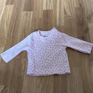 Rosa prickig långärmad tröja från I Love Eco - Söt rosa långärmad tröja med prickigt mönster från I Love Eco. Tillverkad i mjukt material med praktiska knappar vid axeln för enkel påklädning. Perfekt för de små!