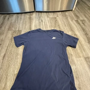 Mörkblå t-shirt från Nike - Säljer en mörkblå t-shirt från Nike med korta ärmar och en liten Nike-logga på bröstet. Perfekt för en avslappnad stil.
