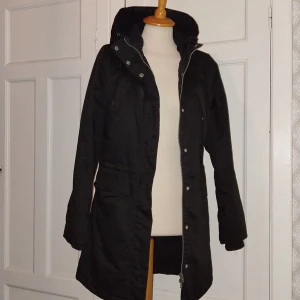 Svart parkajacka med huva - Snygg svart parkajacka från 157 med huva och dragkedja. Jackan har långa ärmar och är perfekt för kyligare väder. Insidan är fodrad för extra värme.