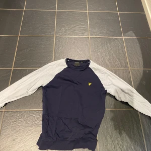 Mörkblå tröja med ljus blå ärmar från Lyle & Scott - Snygg mörkblå tröja från Lyle & Scott med kontrasterande ljus blå ärmar. Tröjan har en gul logotyp på bröstet och är perfekt för en avslappnad stil. Passar bra till jeans eller chinos.
